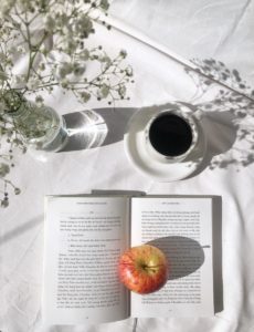 apple fruit on top of open book beside black coffee in white ceramic cup on table